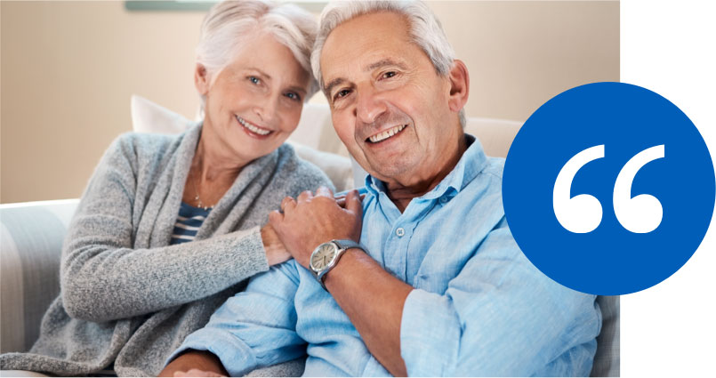 testimonials Smiling elderly couple sitting on a couch with a blue testimonial quotation icon.