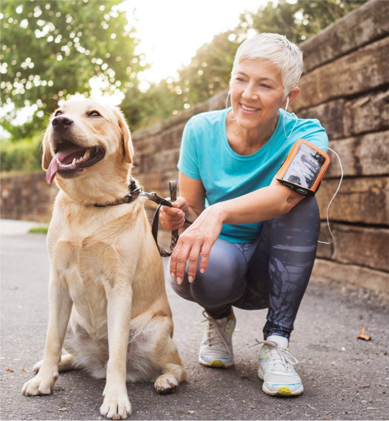 senior-with-dog Senior person with short hair crouches and holds a leash attached to a happy dog during a walk.