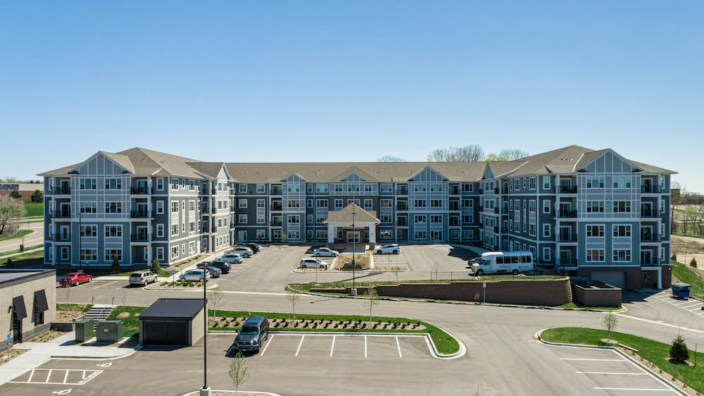 Aerial view of a large, modern apartment building with parking spaces and clear blue sky.
