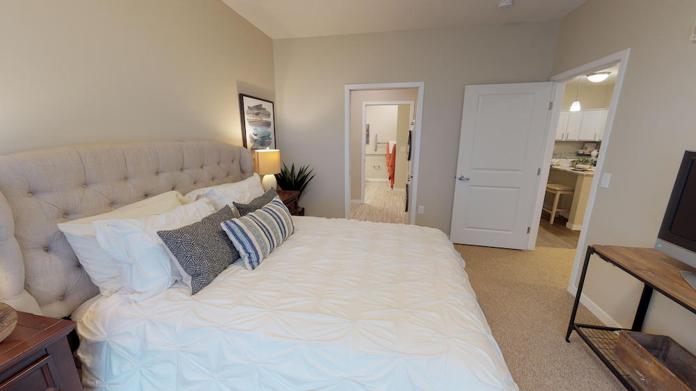 Bedroom with a large bed, decorative pillows, and a view into the bathroom and kitchen