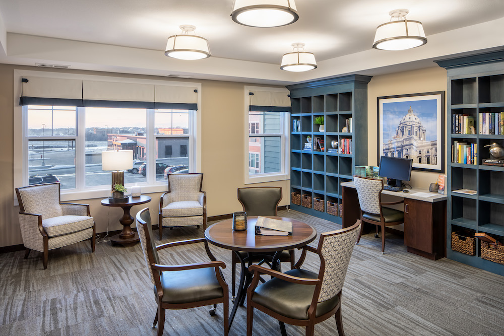Cozy study room with bookshelves, computer desk, round table, chairs, and large window with city view.