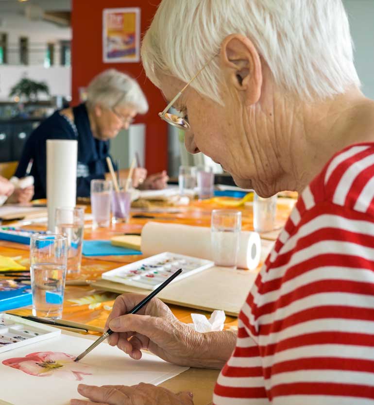 senior-painting Elderly woman painting a pink watercolor flower in art class