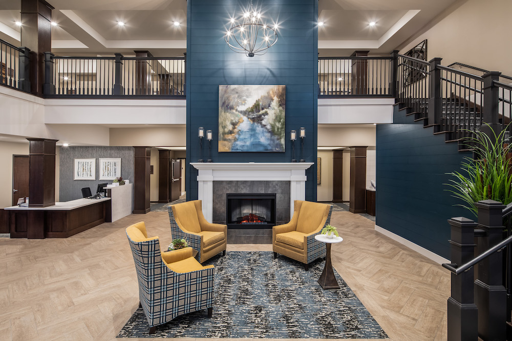 Elegant lobby with fireplace, chandelier, and three chairs around a table on a decorative rug.