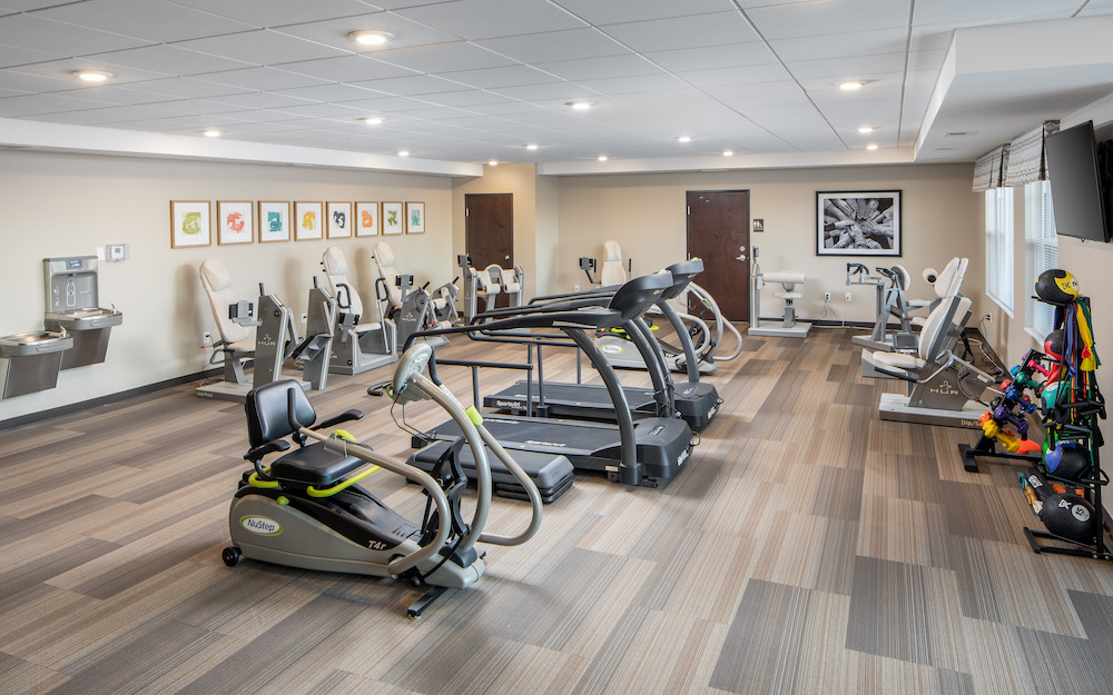 A modern gym with various exercise equipment including treadmills, ellipticals, and weight machines.