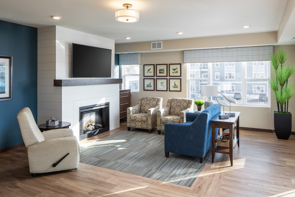 Bright modern living room with fireplace, TV, armchairs, and large windows.