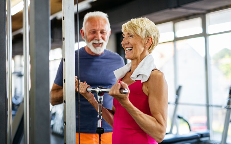 Two seniors exercising with weights at the gym, smiling and having a great time together.