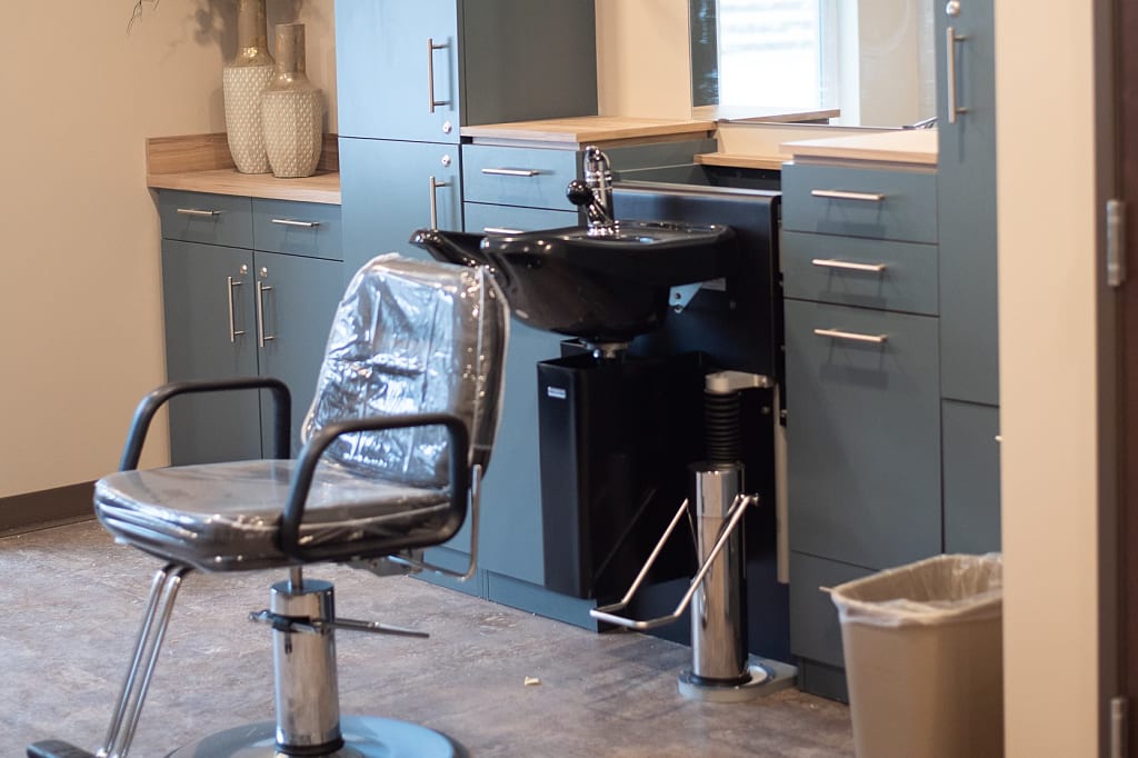 Hair salon station with chair and hair washing sink around cabinets.