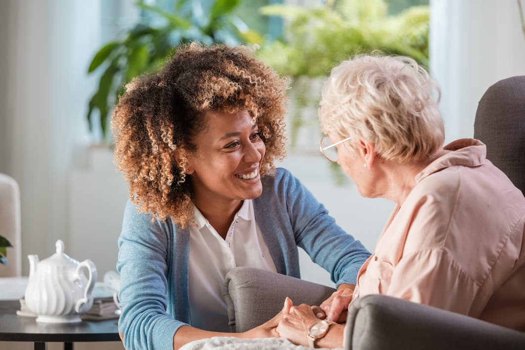 Senior woman speaking to caregiver while holding hands
